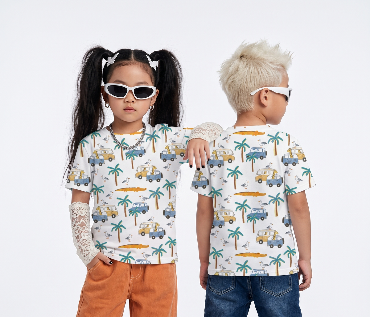 Two children modeling matching short-sleeve t-shirts with a white base and a colorful tropical car-and-palm-tree print, photographed against a clean light gray studio background.